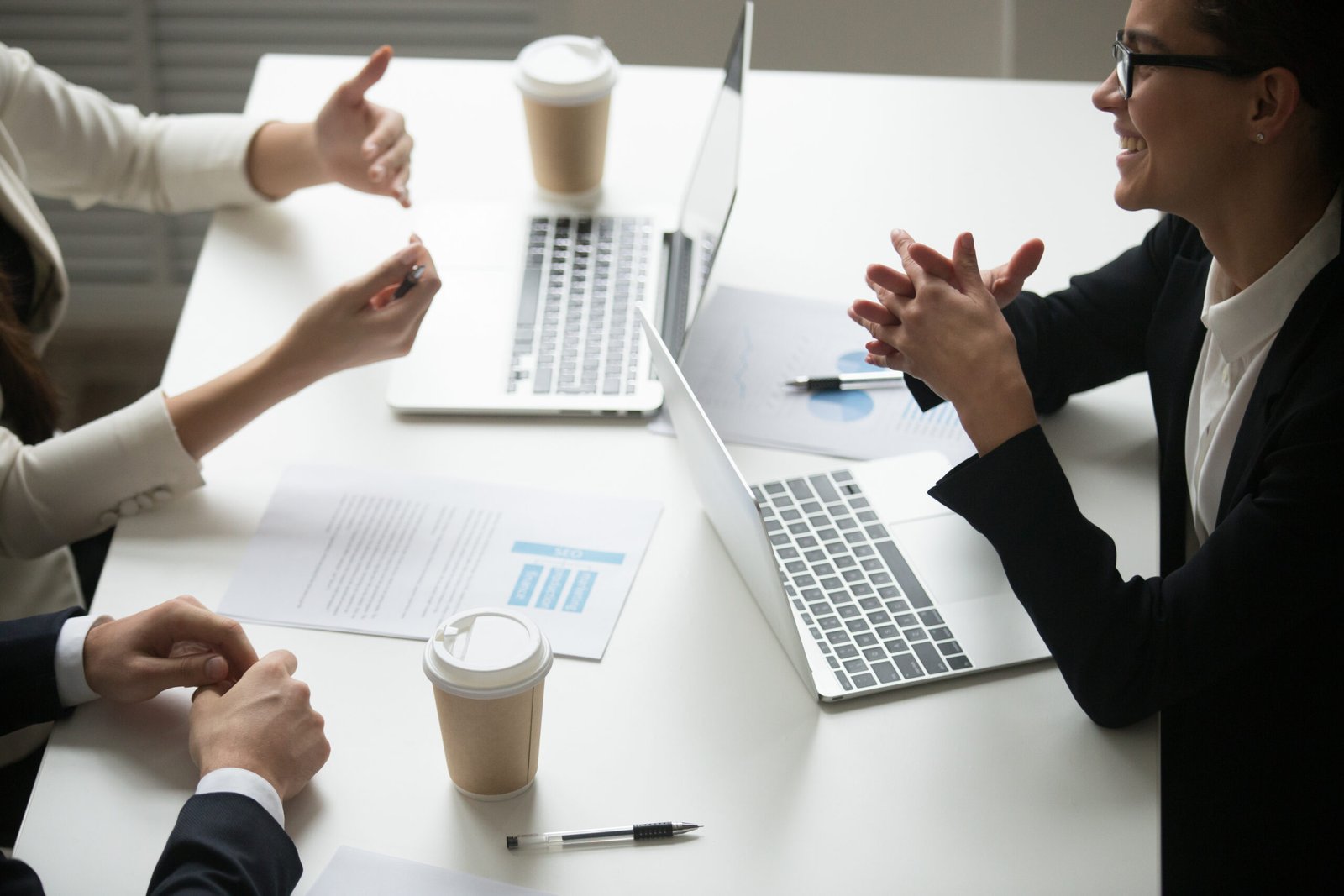 Smiling businesswoman enjoying talk to colleagues during teamwork with laptops, project team laughing working together at meeting, happy business people group have fun pleasant conversation in office