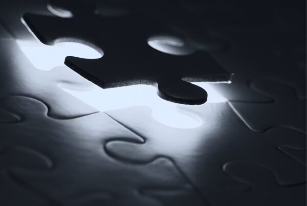 A dark puzzle piece hovering over a glowing gap in a mostly dim jigsaw.