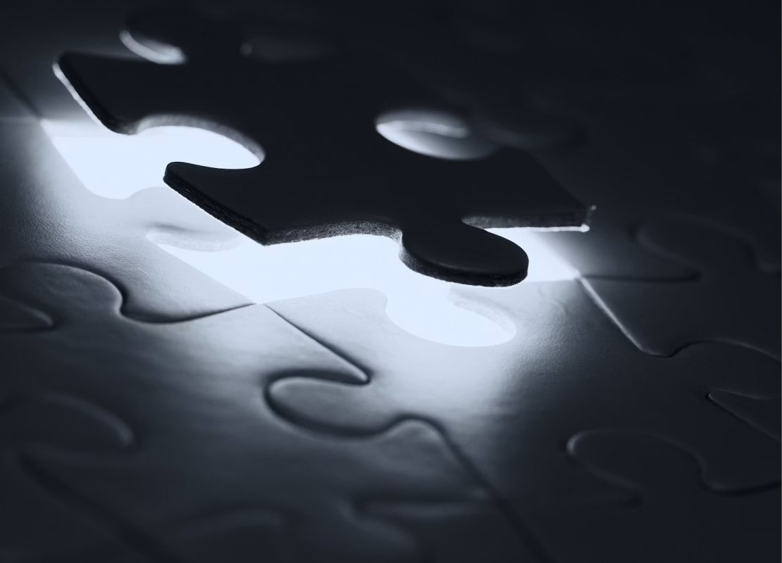A dark puzzle piece hovering over a glowing gap in a mostly dim jigsaw.