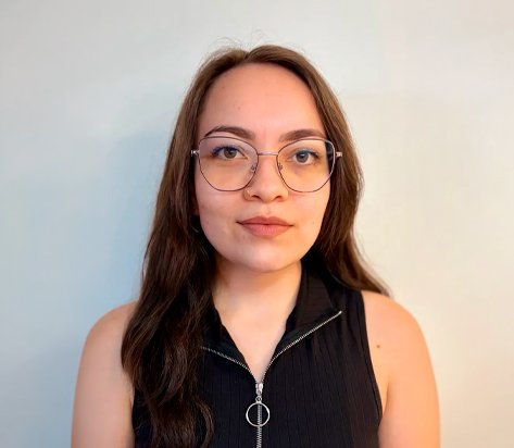 Portrait of a woman with long brown hair and round glasses, wearing a sleeveless black zip-up top, looking at the camera with a neutral expression.