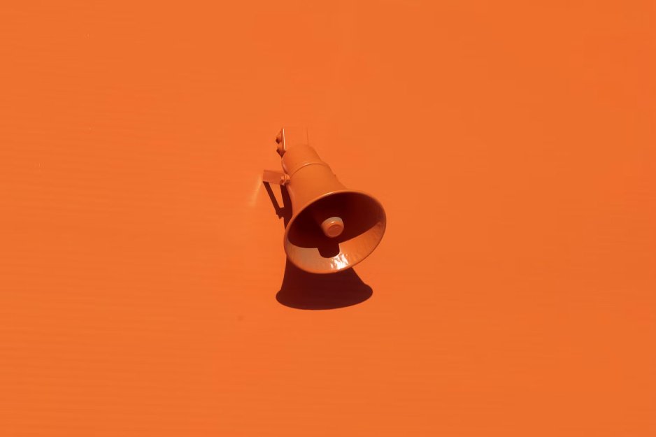 Orange megaphone mounted on an orange background, casting a shadow below.