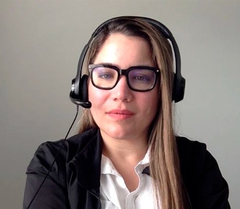 Woman wearing a black headset with microphone, looking at the camera in a business setting with a white blouse and black blazer