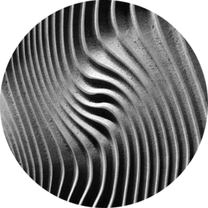 Close-up of wavy striped patterns in sand or fine material, creating an abstract textured surface in grayscale.