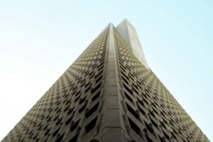 Low-angle shot of a tall triangular concrete skyscraper with a perforated grid facade against a light blue sky.