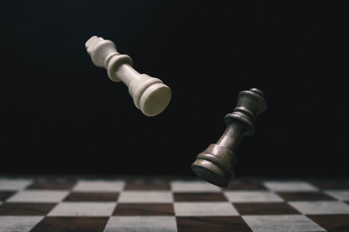 White and black chess kings tumbling midair above a checkered chessboard.