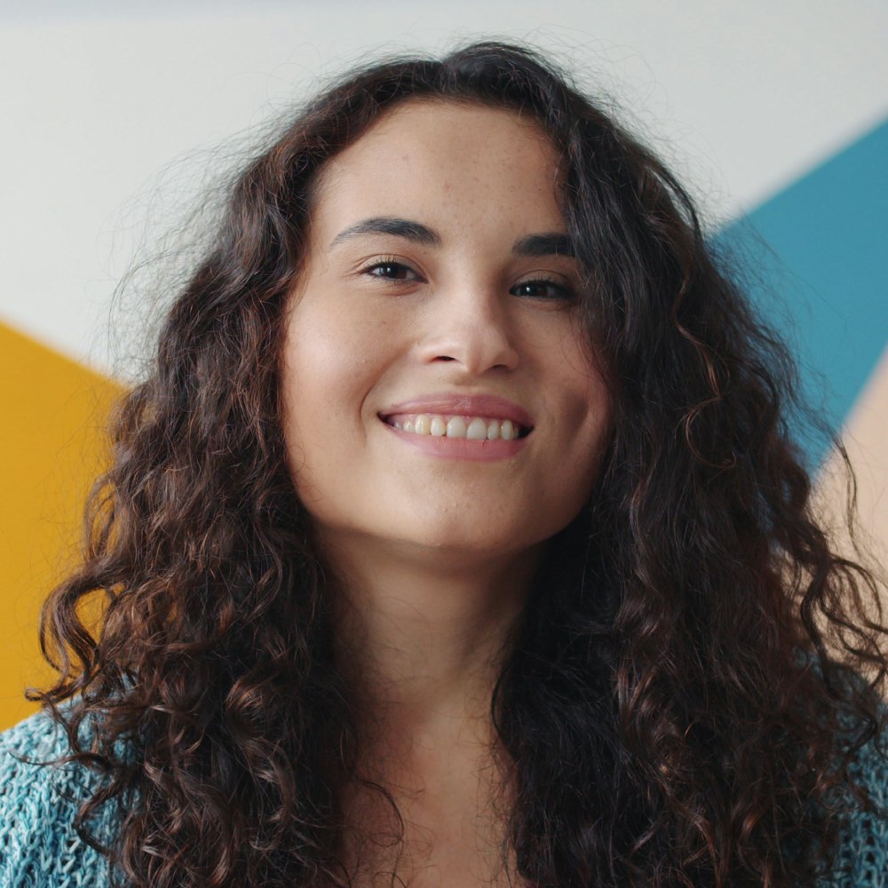 Smiling woman with long, curly dark hair in front of a colorful geometric backdrop.
